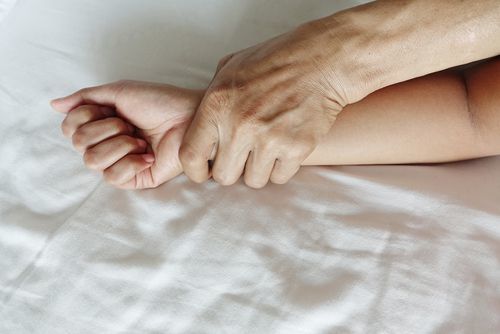 mano de hombre sujetando la mano de una mujer en la cama como ejemplo de agresión sexual según Colorado 18-3-402 CRS
