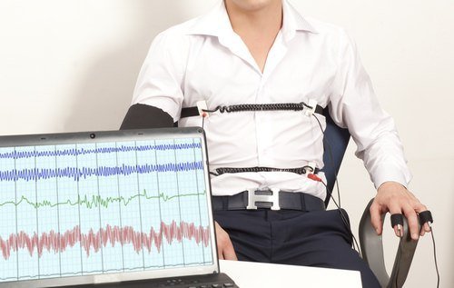 Man strapped to a lie detector machine with the results appearing on a laptop in front of him