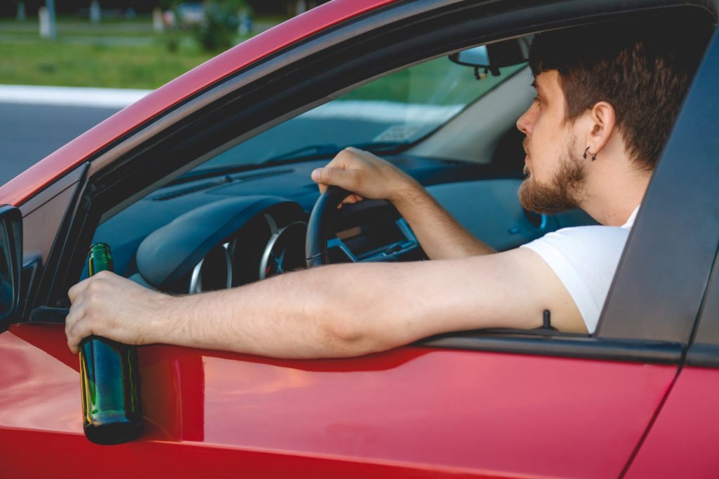 Driver holding beer bottle while on the road during the daytime