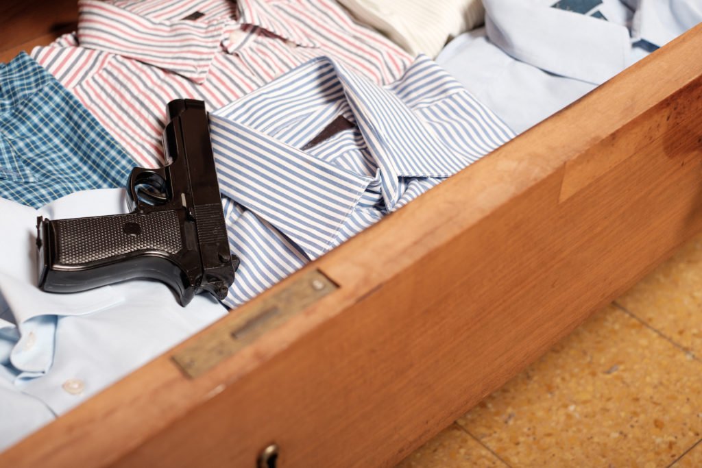 Revólver en un cajón abierto de cómoda sobre varias camisas dobladas, lo que cuenta como posesión ilegal por alguien con condena previa por delito grave
