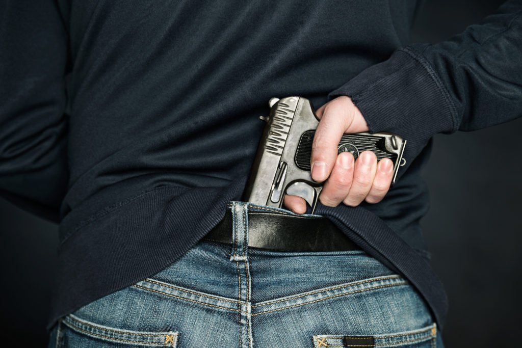 Hombre agarrando un revólver en la cintura trasera como ejemplo de posesión de un arma por un infractor previo en Colorado