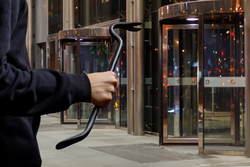 Man holding a crowbar in front of a commercial building as an example of possession of burglary tools in Colorado