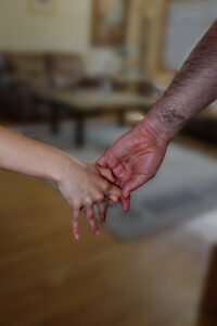 Big hairy man's hand is pulling small girl's hand.