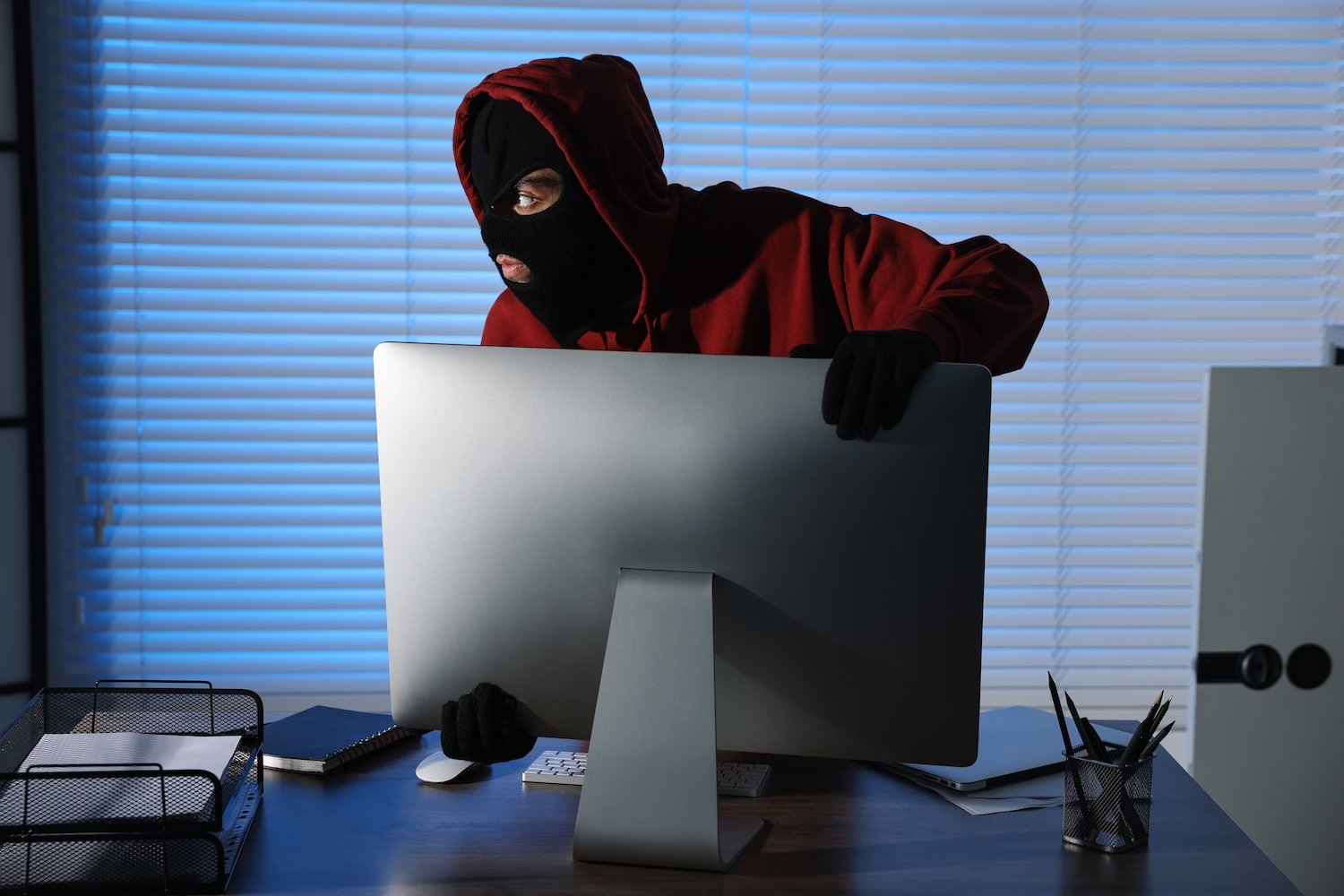 Masked thief in an office stealing a desktop computer