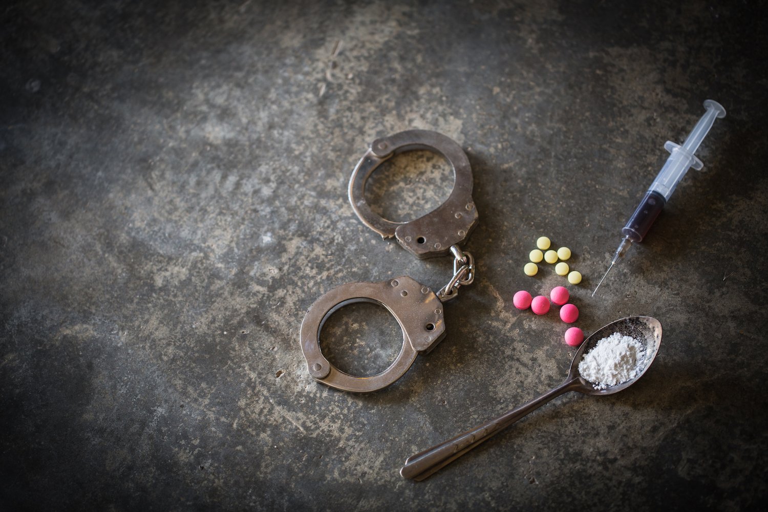 Handcuffs with drugs, heroin, and a needle on a table