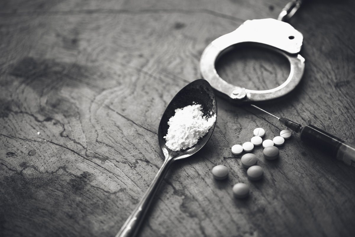 Handcuffs, a heroin spoon, and pills on a table
