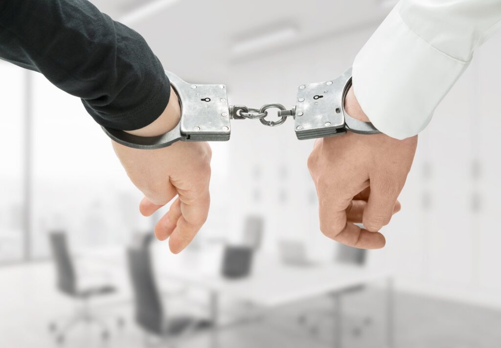 Closeups of handcuffs tethering the hands of two different people together to illustrate two accomplices to a crime