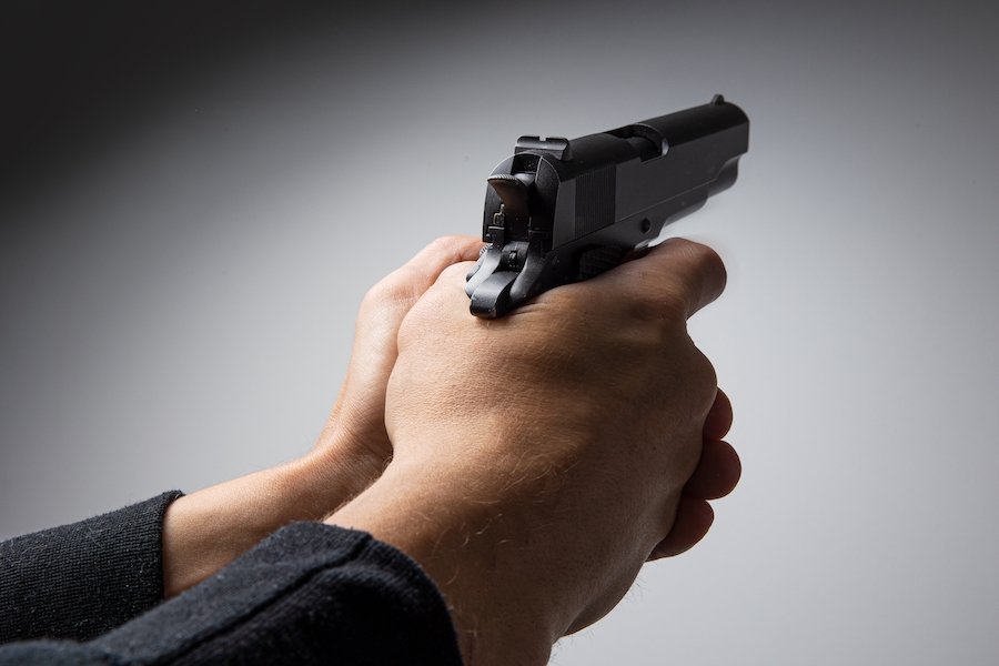 Close-up of hands holding a gun against a grey background