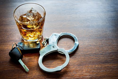Closeup of a tumbler of whiskey, handcuffs, and car keys on a wooden table