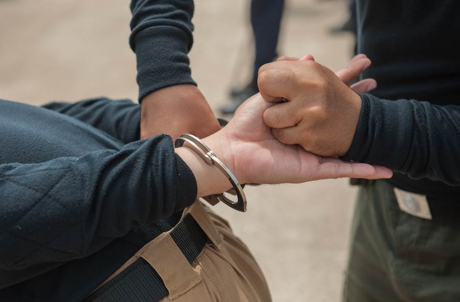 Closeup of plainclothes officer handcuffing arrestee after violating CRS 18-8-103, with the pavement in the background