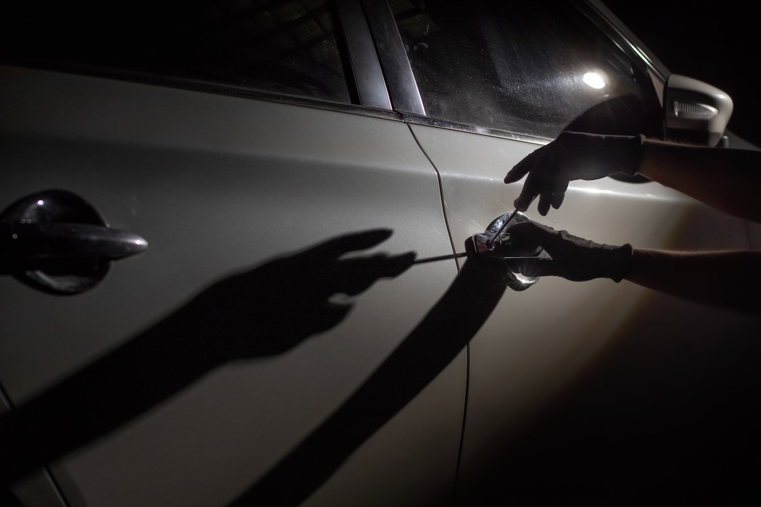 Thief's gloved hands stealing a sedan at night