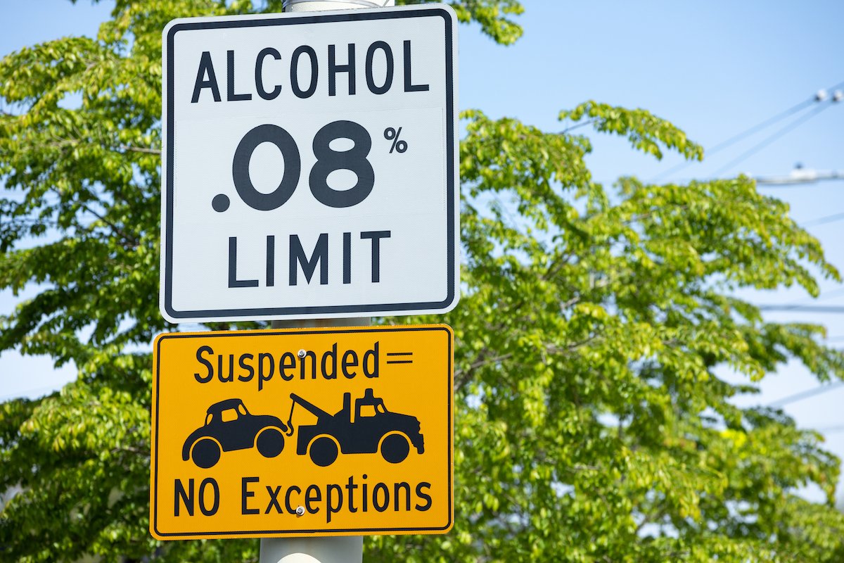 Traffic sign that says "Alcohol .08% limit, Suspended, No exceptions" against a tree and blue sky