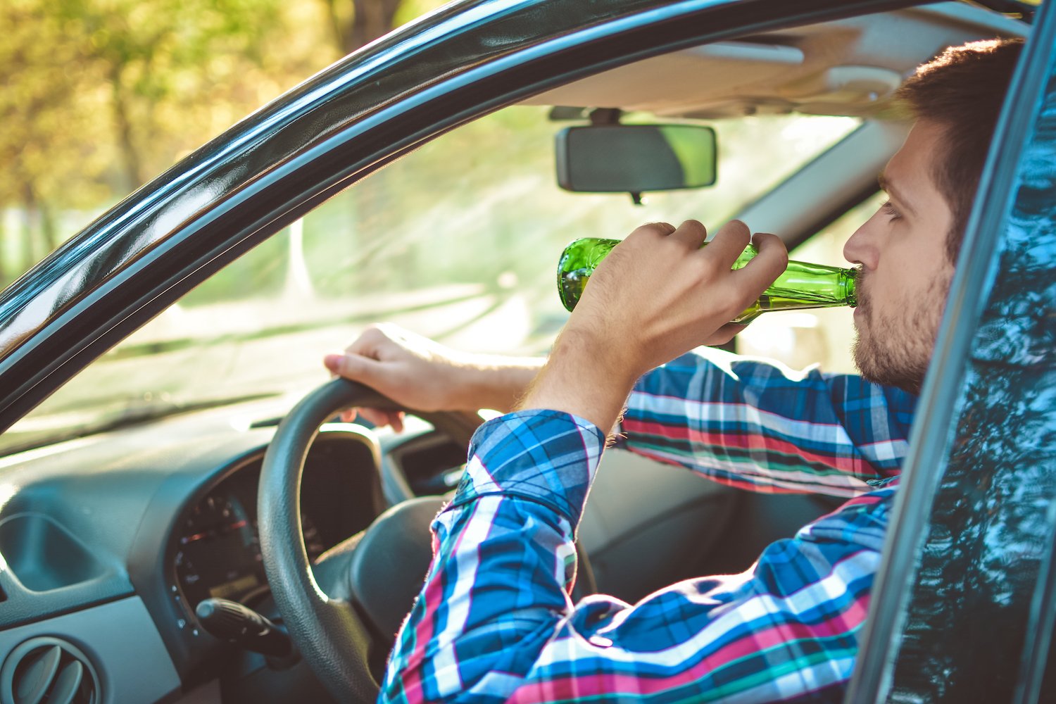 Man driving a sedan while drinking a beer bottle during the day