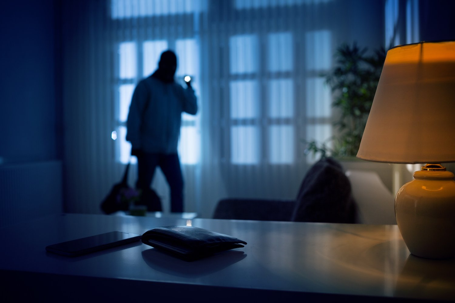 Burglar inside of a house with flashlight trained on a wallet on a desk