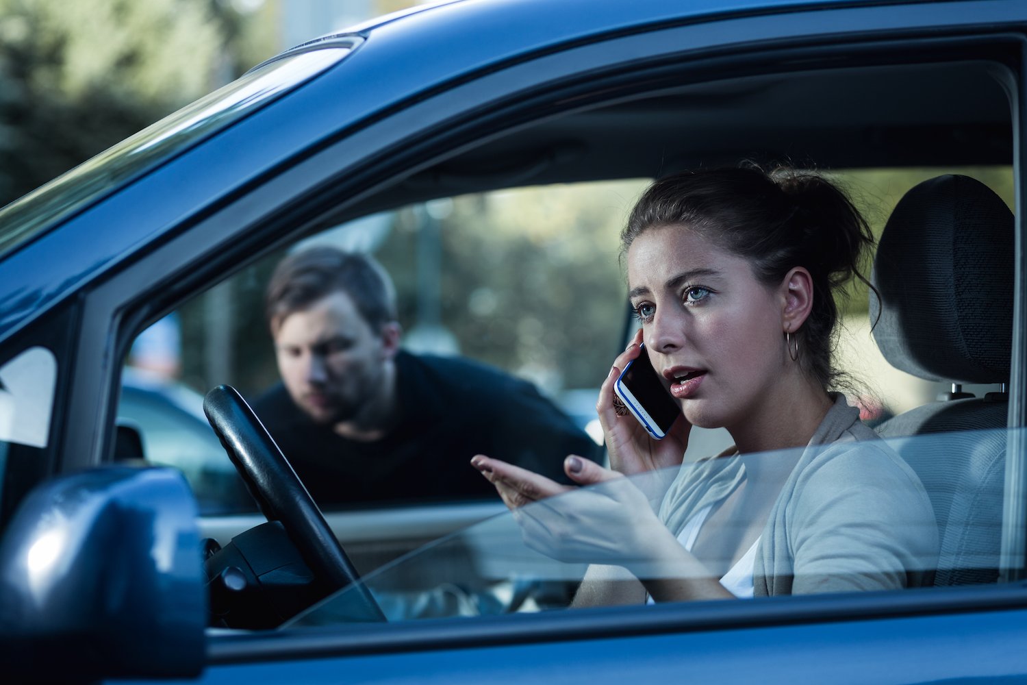 Woman talking on phone in her car while a man stalks her through a window