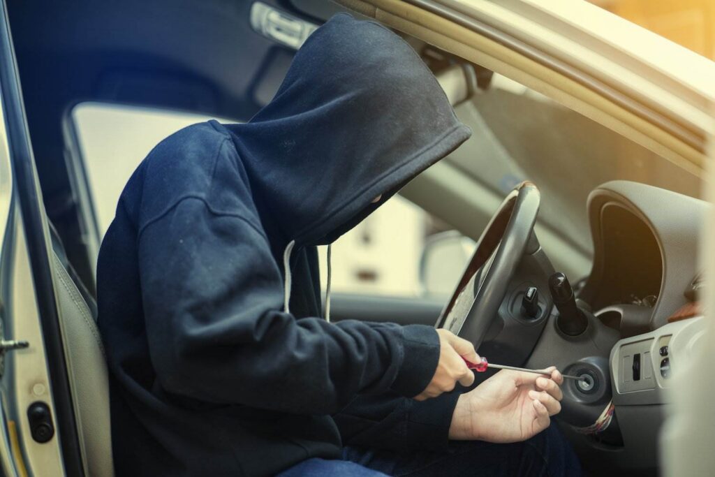 Hooded thief sitting in driver's seat trying to hot wire a car as an example of a violation of Colorado CRS 18-4-409