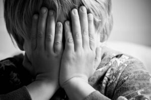 Black and white image of a child sex abuse victim with hands over his face