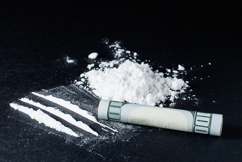 A pile of cocaine next to three lines of coke and a rolled-up $100 bill on a black table