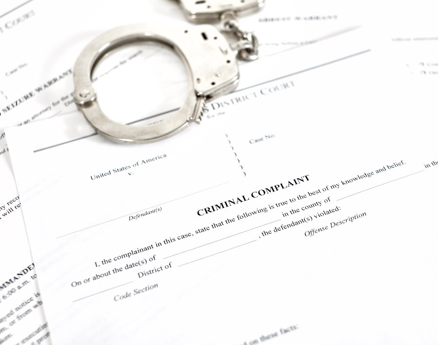 Criminal complaint forms on a table with a pair of handcuffs lying on top of the papers