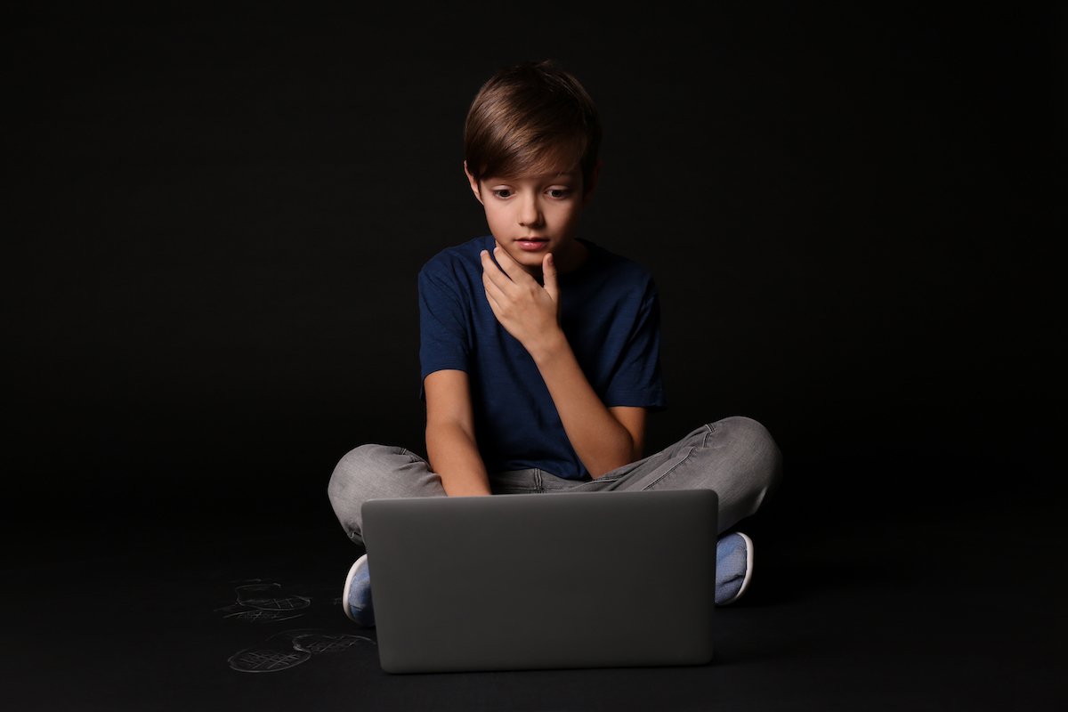 Boy in front of a laptop against a black background
