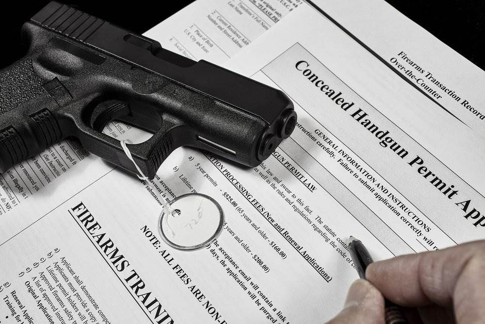 Person filling out a concealed carry application form with a handgun on top of the form