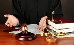 Judge's outstretched hands over a desk with a gavel, scales of justice, and law books