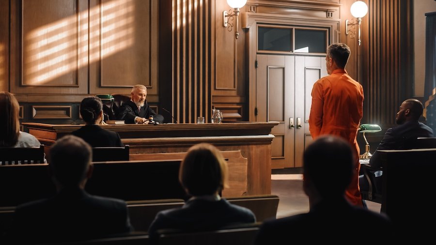 Defendant in orange jumpsuit in a wooden courtroom being sentenced by a judge hammering down a gavel