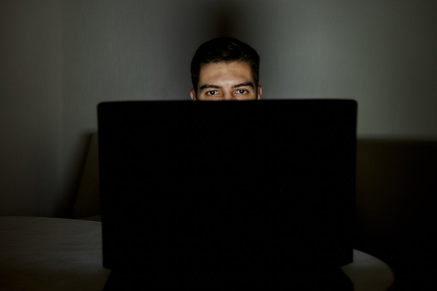 Man looking at laptop presumably containining child porn in violation of CRS 18-6-403, and the room is dark and illuminated only by the light from the computer screen