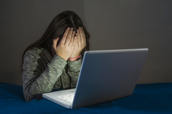 Woman with her head in her hands in front of her computer after being threatened online in violation of CRS 18-9-111
