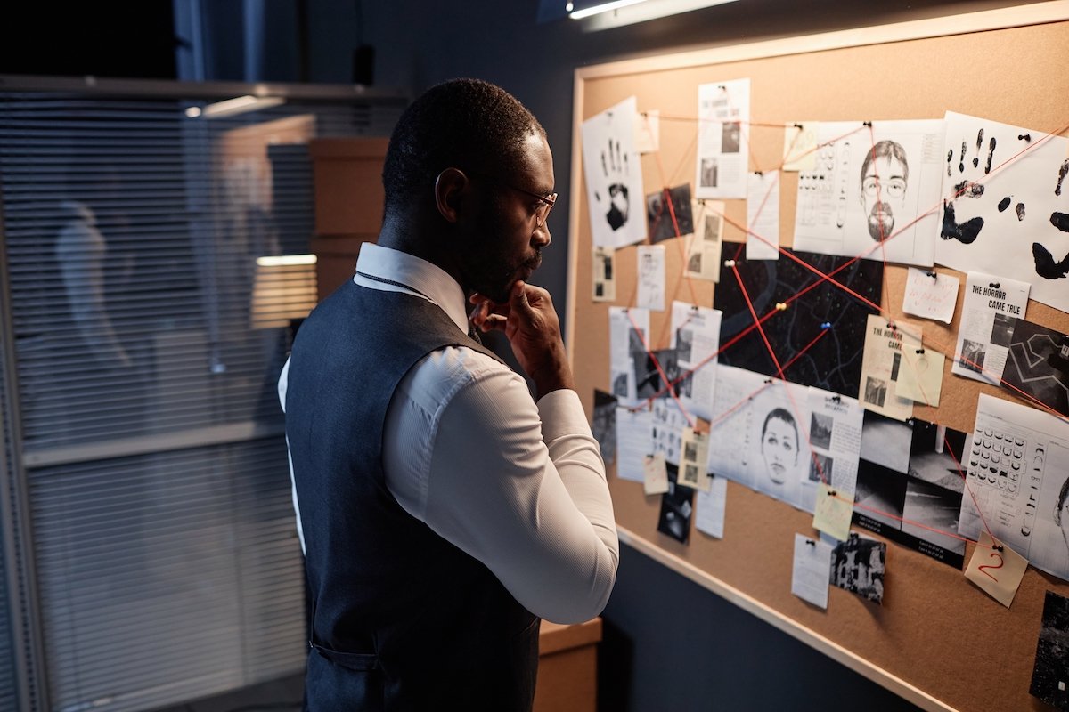 Detective in front of a cork board full of evidence