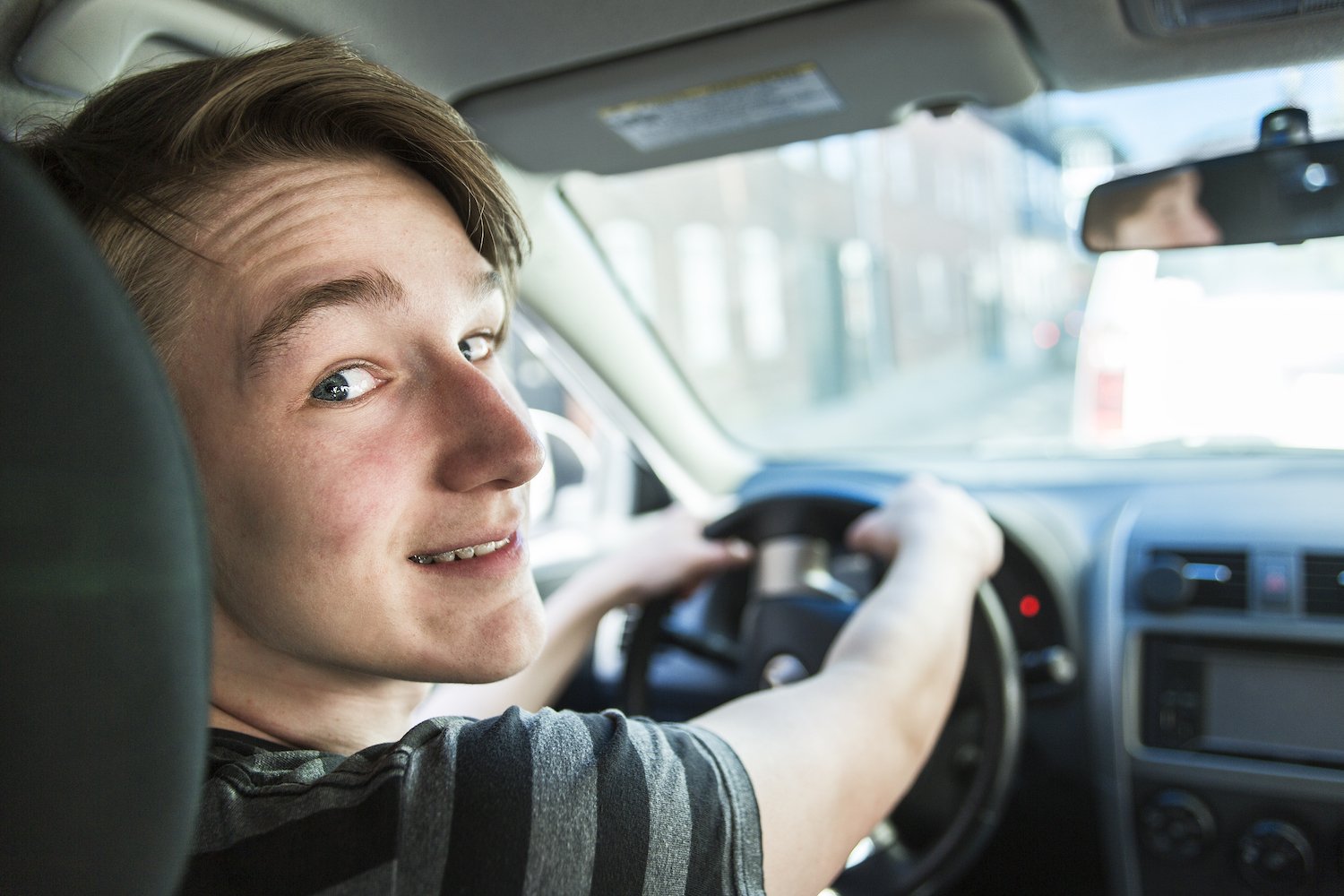 Young driver with acne in the car looking back at the camera