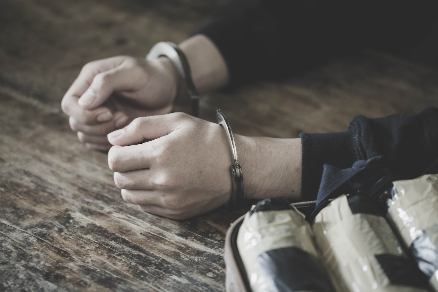 Handcuffed hands on a table next to bundles of confiscated cocaine