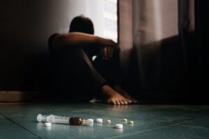 Man in corner on floor with needle and pills