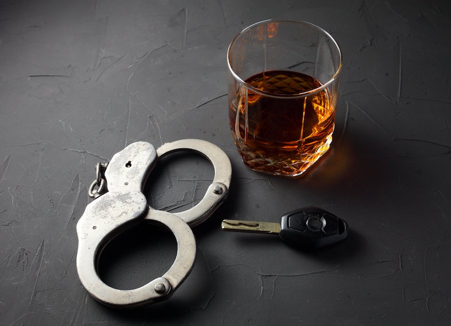 handcuffs, a car key, and a glass of booze on a grey slate table