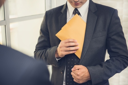 Business man placing envelope in suit jacket pocket as a example of embezzlement of public property per CRS 18-8-407
