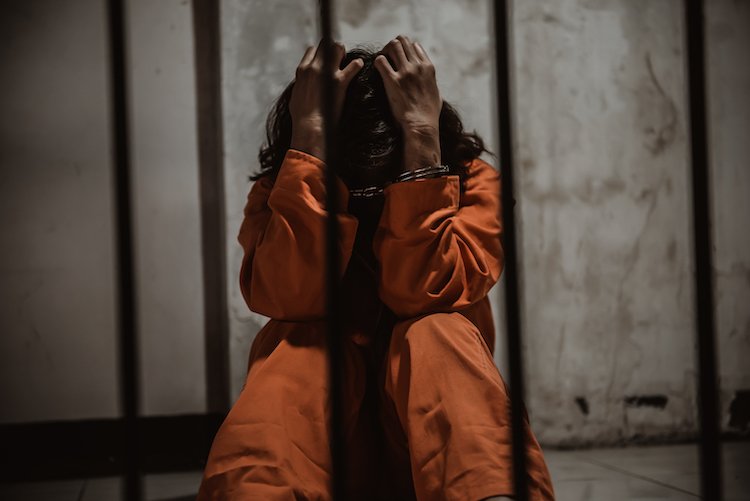 Woman in orange jumpsuit behind bars