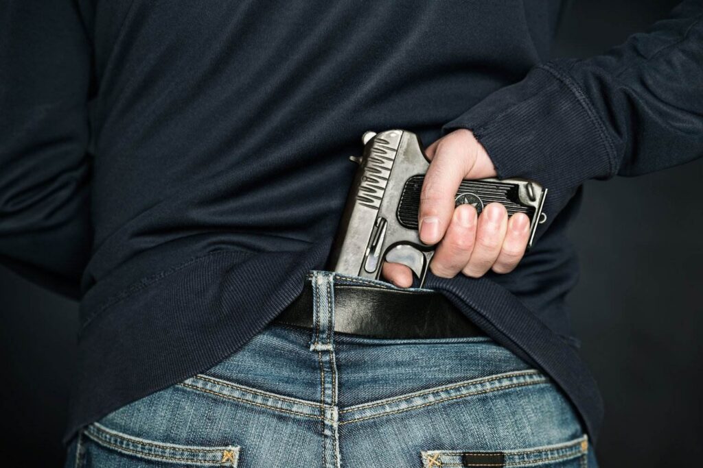 Man gripping a revolver in his back waistband as an example of possession of a weapon by a previous offender in Colorado