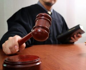 Judge in a black robe hammering gavel during disposition hearing while holding a law book in his other hand
