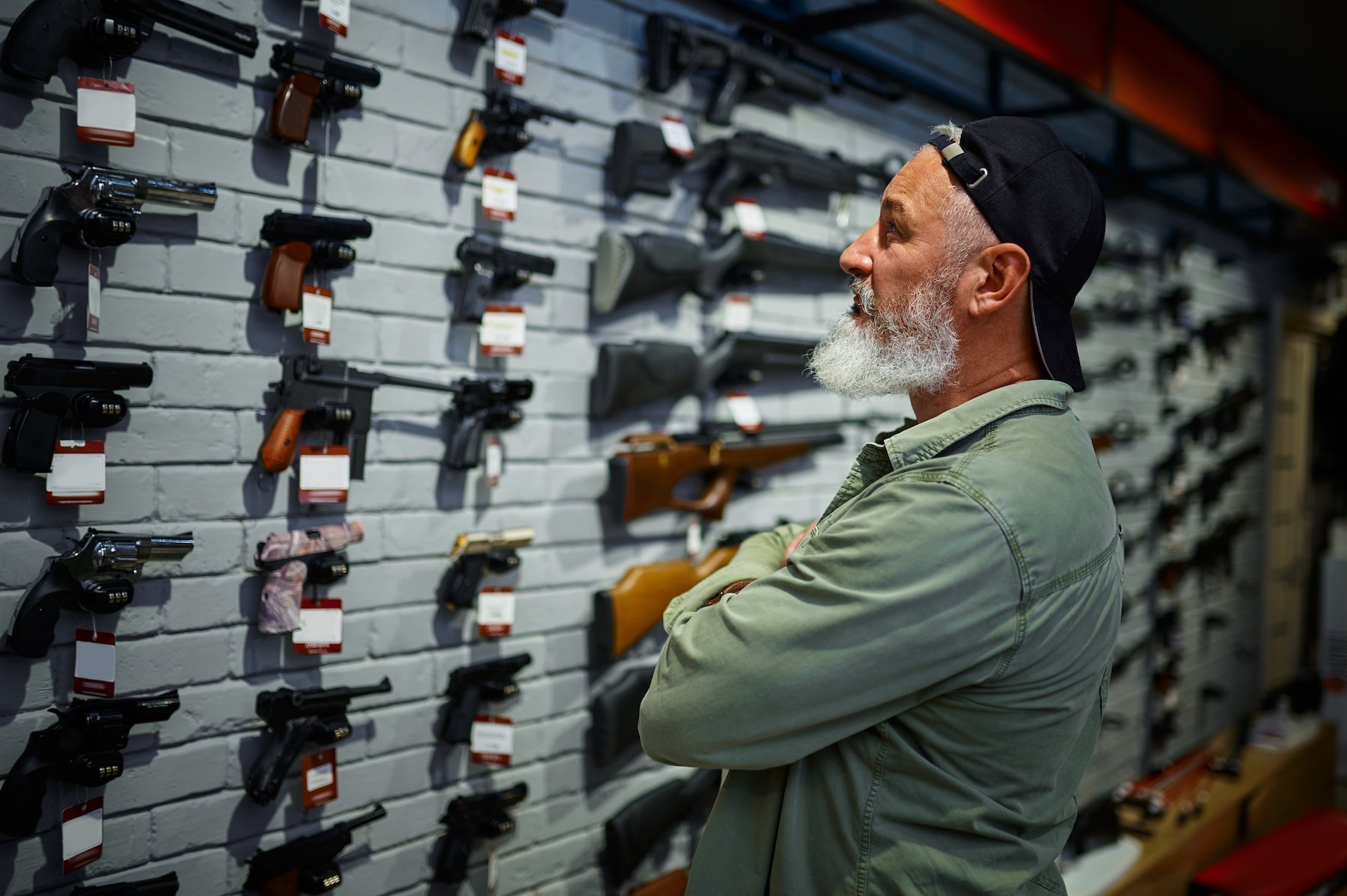 Male customer looking at selection of guns in a gun store displayed on a wall