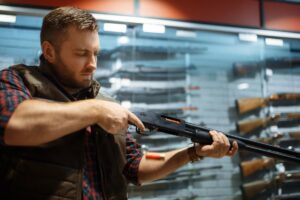 Man at a gun shop holding a rifle he is thinking about buying 