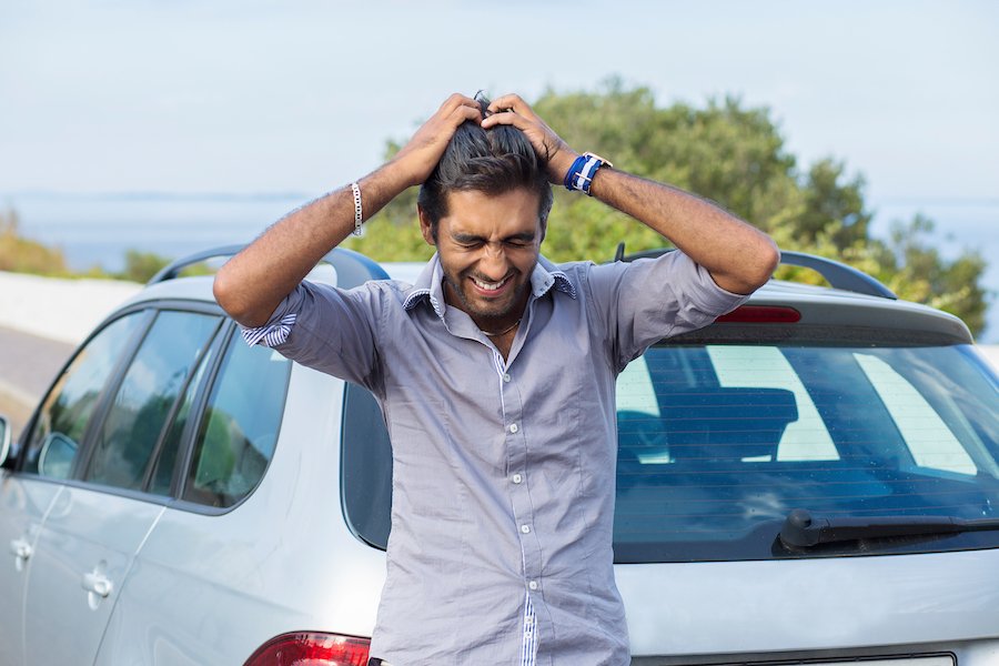 Hit-and-run victim standing on the road outside of his damage sedan holding up his hands in exasperation