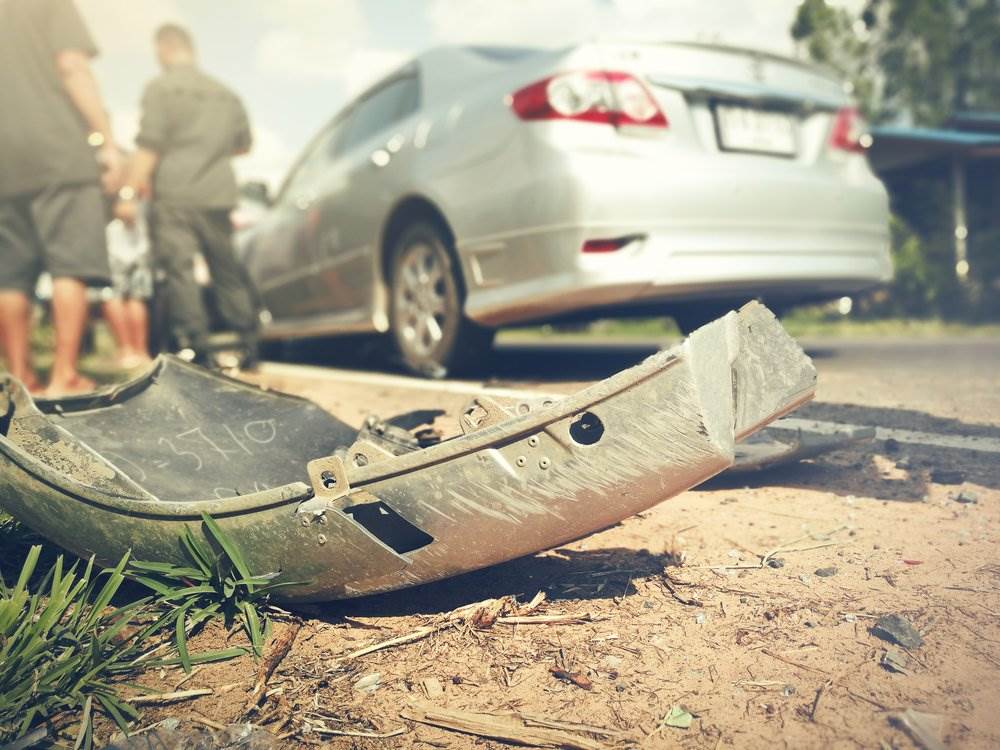 An accident scene with a fallen sedan bumper on the side of the road, and the police is talking to the two drivers involved