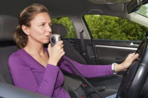 A woman in her car blowing into an IID breathalyzer, which is a typical condition for driving following a DUI in Colorado