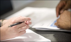 Hand holding pen over pile of papers