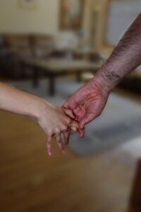 Big hairy man's hand is pulling small girl's hand.