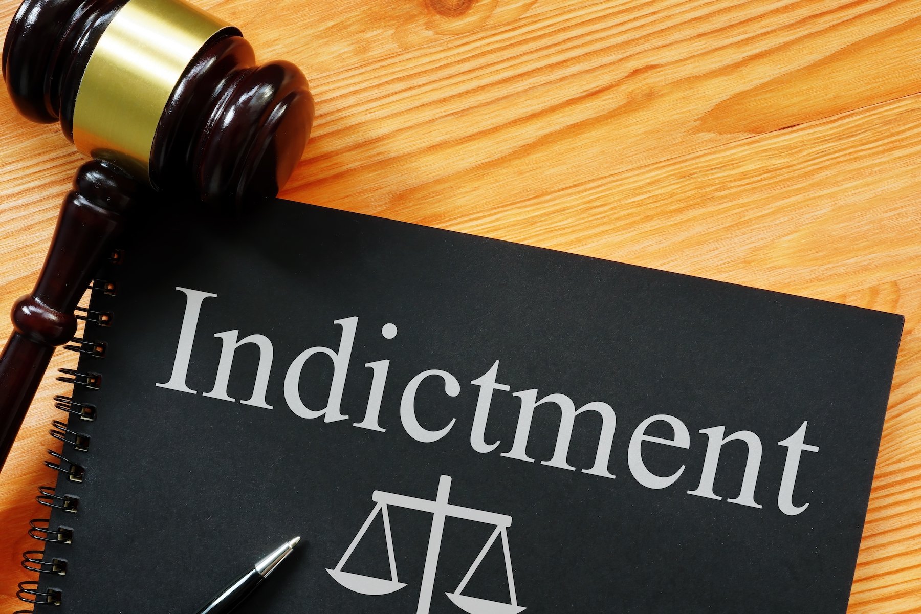 Law book that says "indictment" next to a gavel on a wooden table