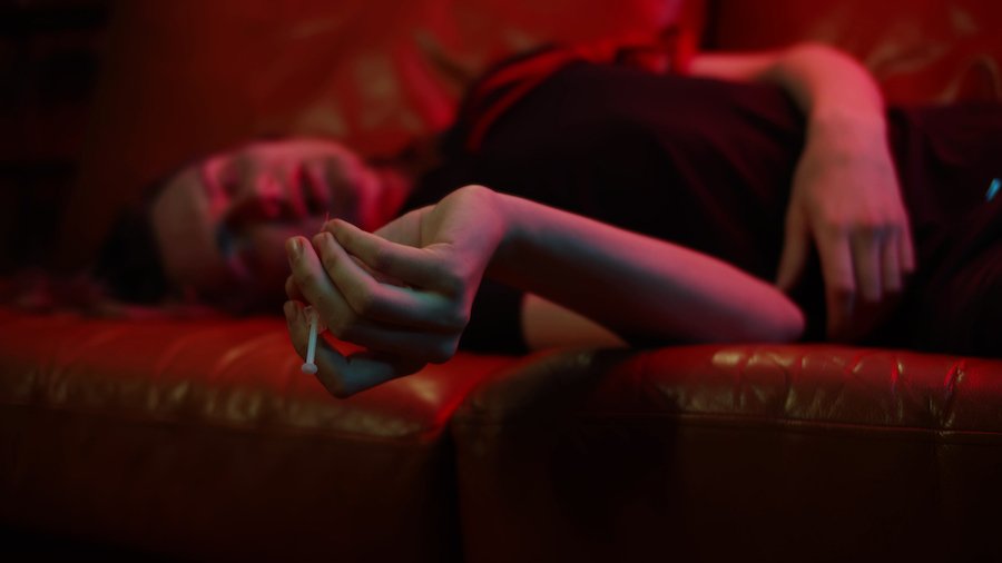 Man on couch holding syringe with heroin in order to get high, which is not the same as being insane