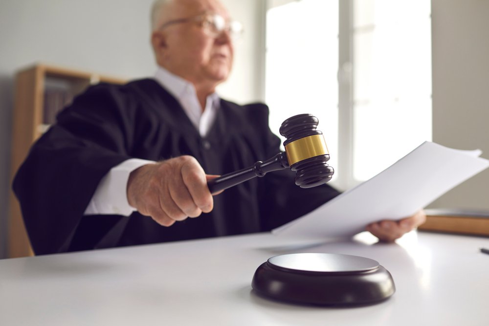 A judge at the bench holding documents in one hand and hammering down a gavel with the other