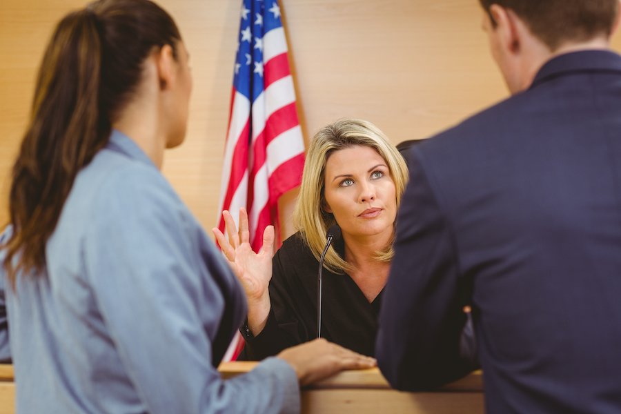 A judge at the bench speaking to defense attorney and a prosecutor during a court hearing