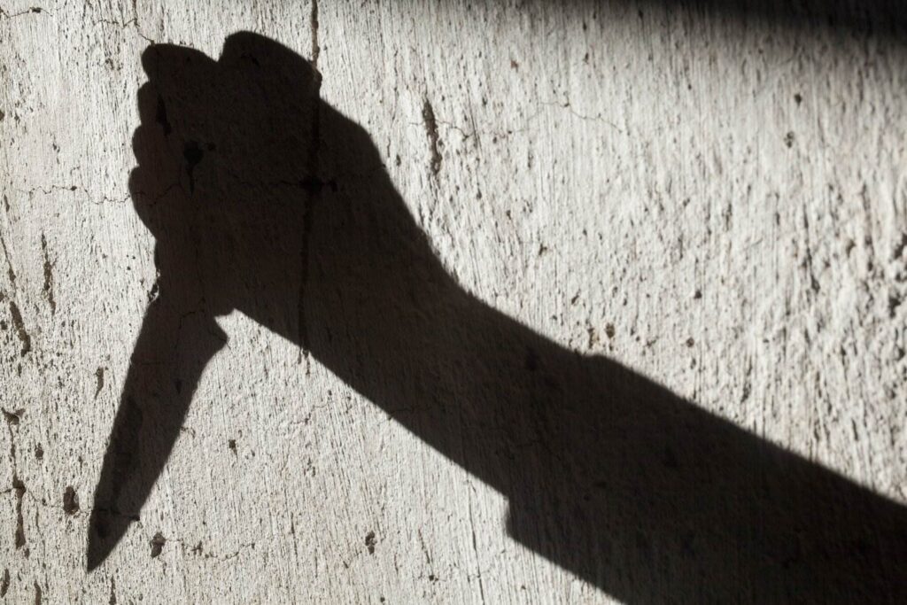 Shadow of a hand wielding knife cast on a concrete wall